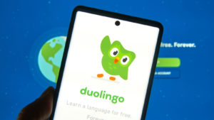 DUOL stock: A phone displaying the duolingo logo in front of a computer screen displaying the duolingo site